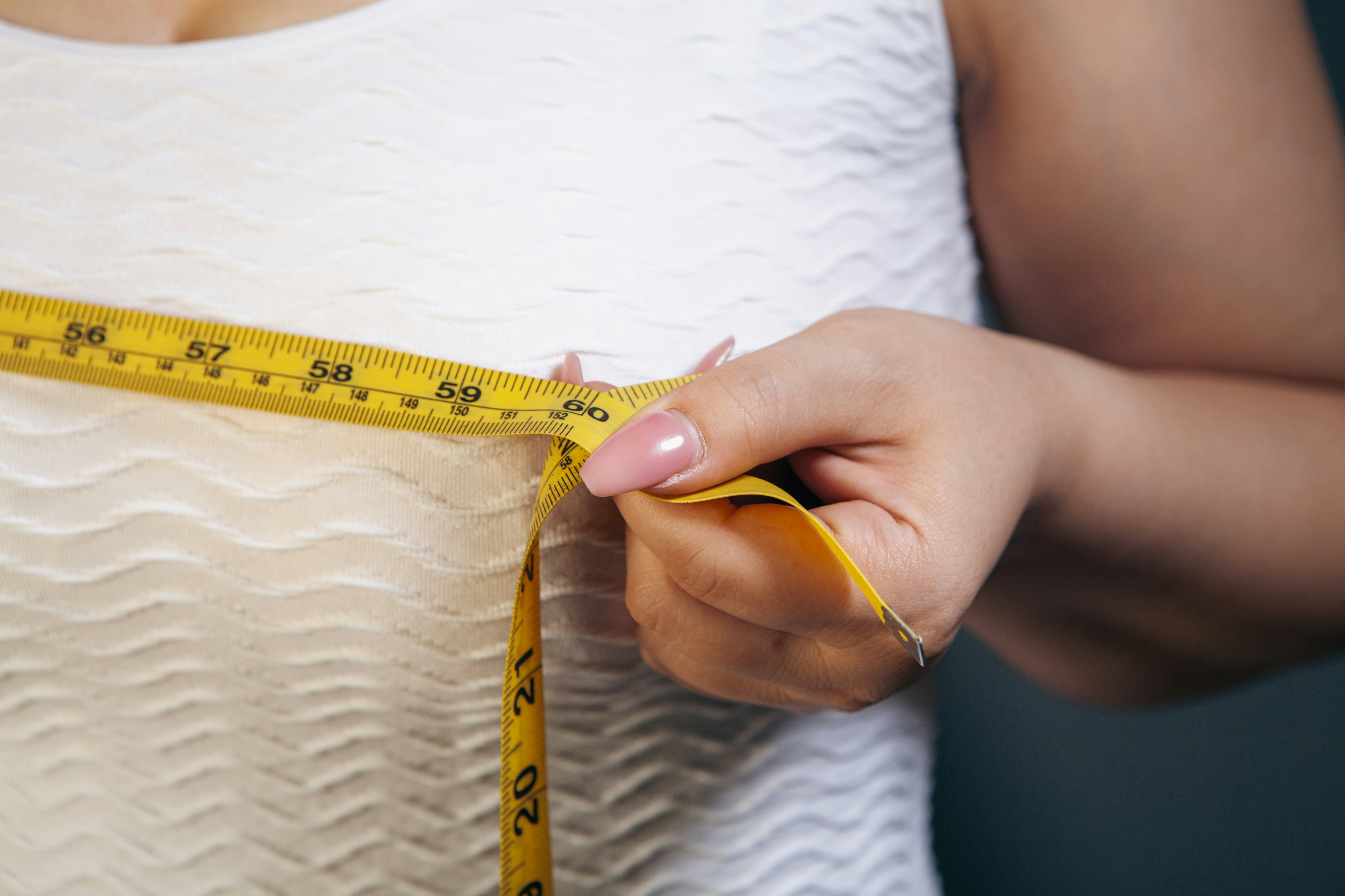 Close-up of a woman measuring her chest with a tape measure.